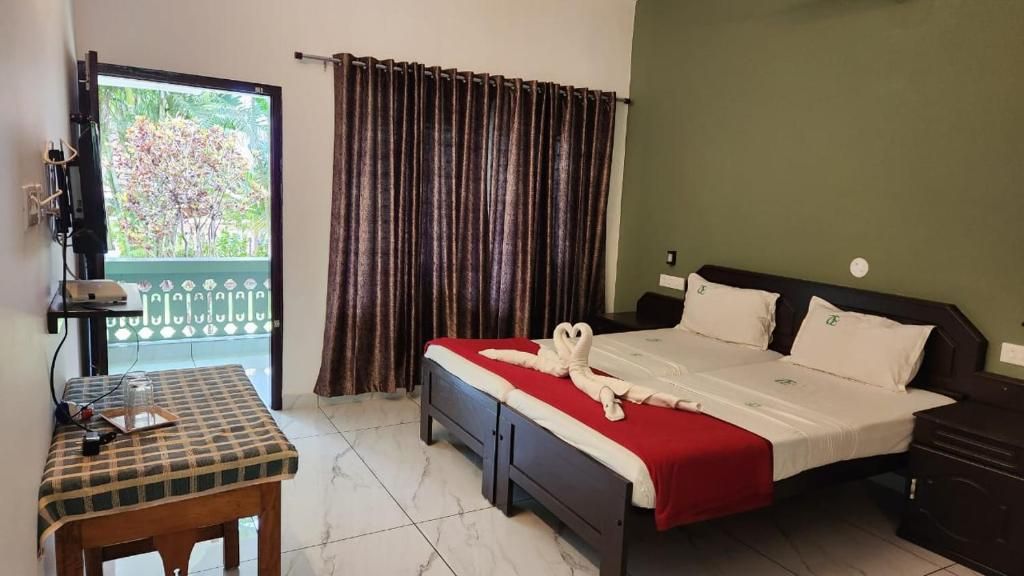 A hotel room with a bed, a small table, a TV, and a view of greenery outside.