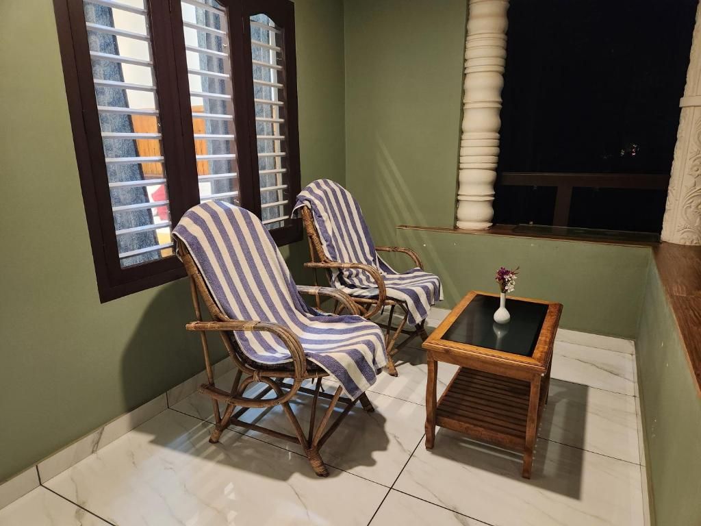 A balcony with wicker chairs and a small table, a window with blinds, and a view of the night sky.