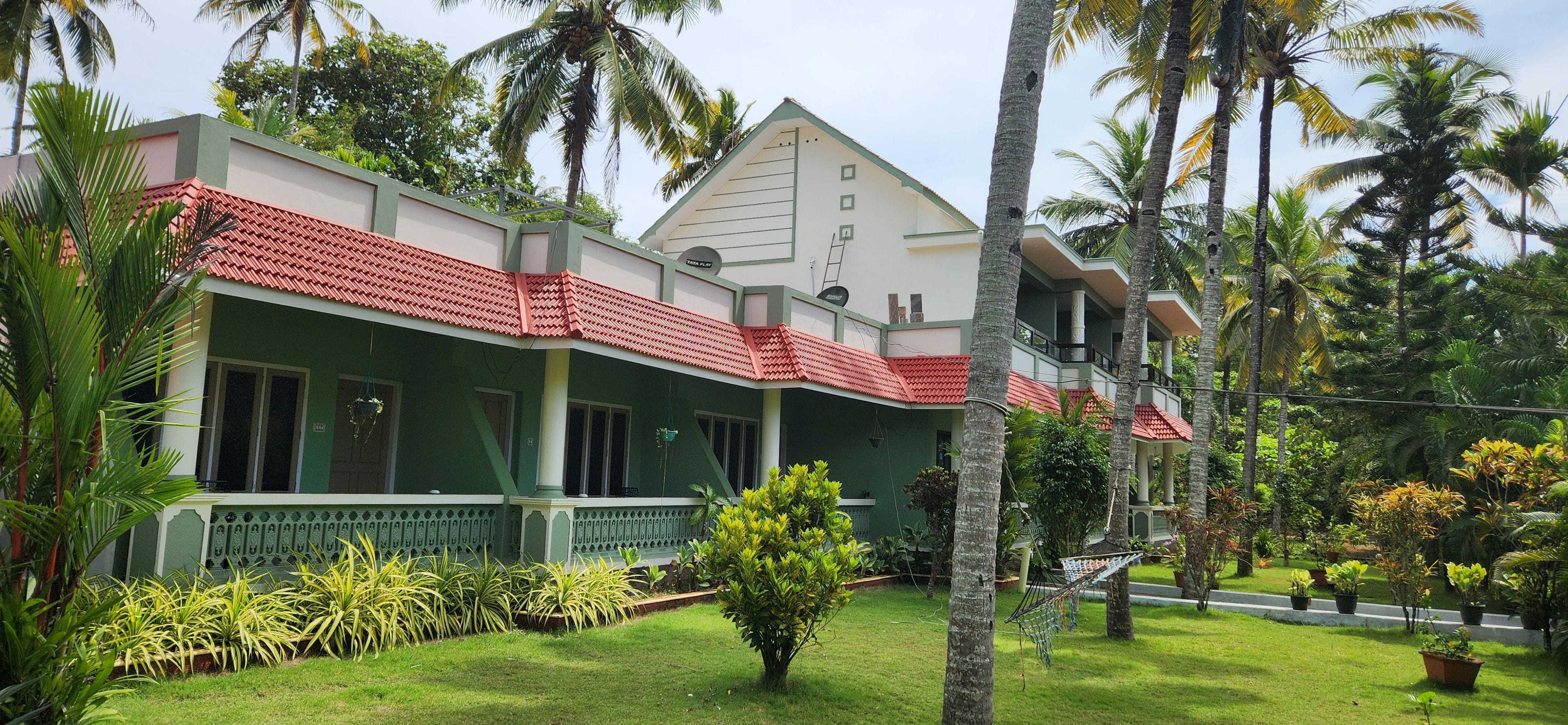 A two-story building with a red-tiled roof, surrounded by lush greenery and palm trees.
