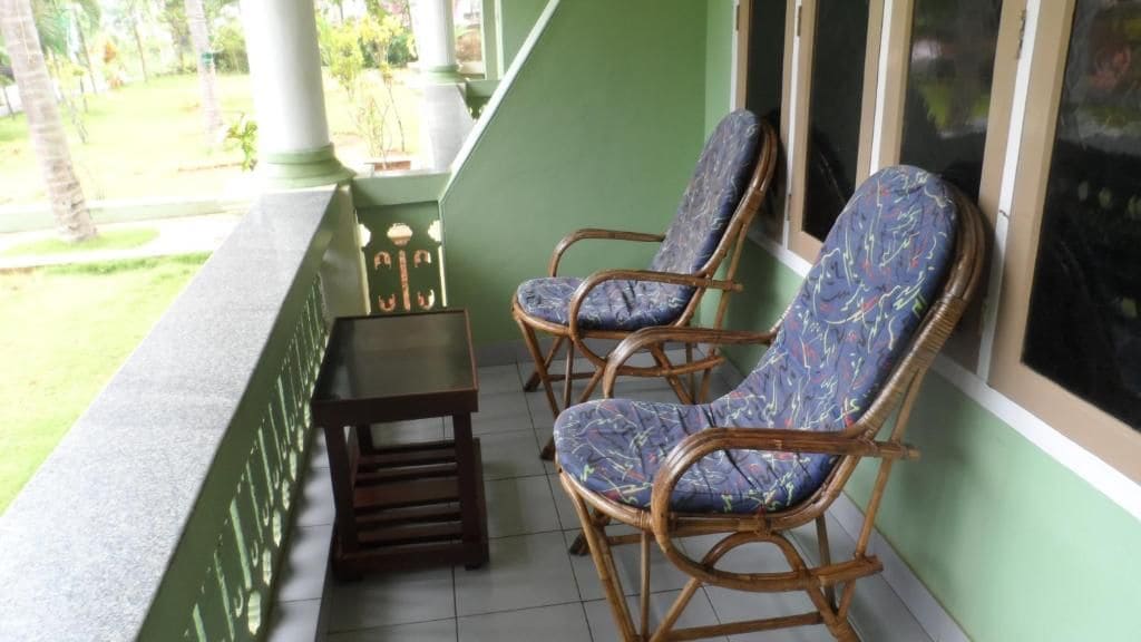 Un balcón con dos sillones de mimbre y una mesita, con vistas a un jardín.