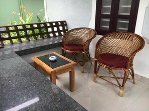 A seating area with two wicker chairs and a small wooden table with a black surface.