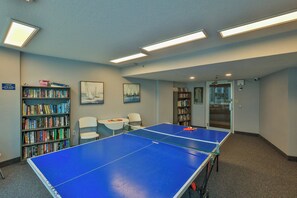 A room with a ping pong table, two chairs, and two bookshelves filled with books. - Peck7NE Oceanfront Condo - Magical Views, Heated Pool, Hot Tub, Beach Decor (Daytona Beach)