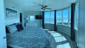 Ein Schlafzimmer mit einem großen Bett, einem Deckenventilator, einem Fernseher und Blick aufs Meer.