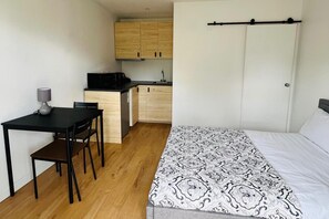 Una habitación funcional con cama, escritorio, silla, kitchenette pequeño y armario.