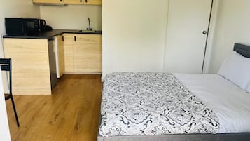 Et kompakt værelse med seng, et lille tekøkken med mikroovn og et træskab.