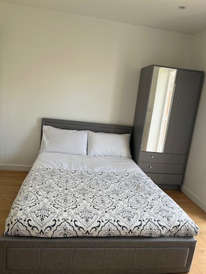 A bed with a patterned bedspread, a grey headboard, and a grey wardrobe with drawers. - Studio Sleeps 2 With Garden and Parking (London)