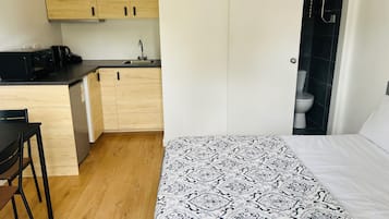 A compact room with a kitchenette, a bed with patterned bedding, and a toilet in the adjacent bathroom.