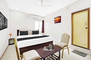 Habitación de hotel con una cama, un escritorio con hervidor, una silla, una puerta con diseño decorativo y un cuadro en la pared.
