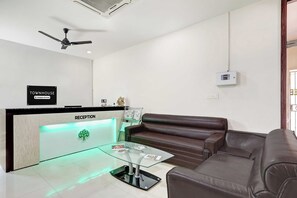 Un área de recepción con mostrador, ventilador de techo, sofá de cuero marrón y una mesa de centro de vidrio.