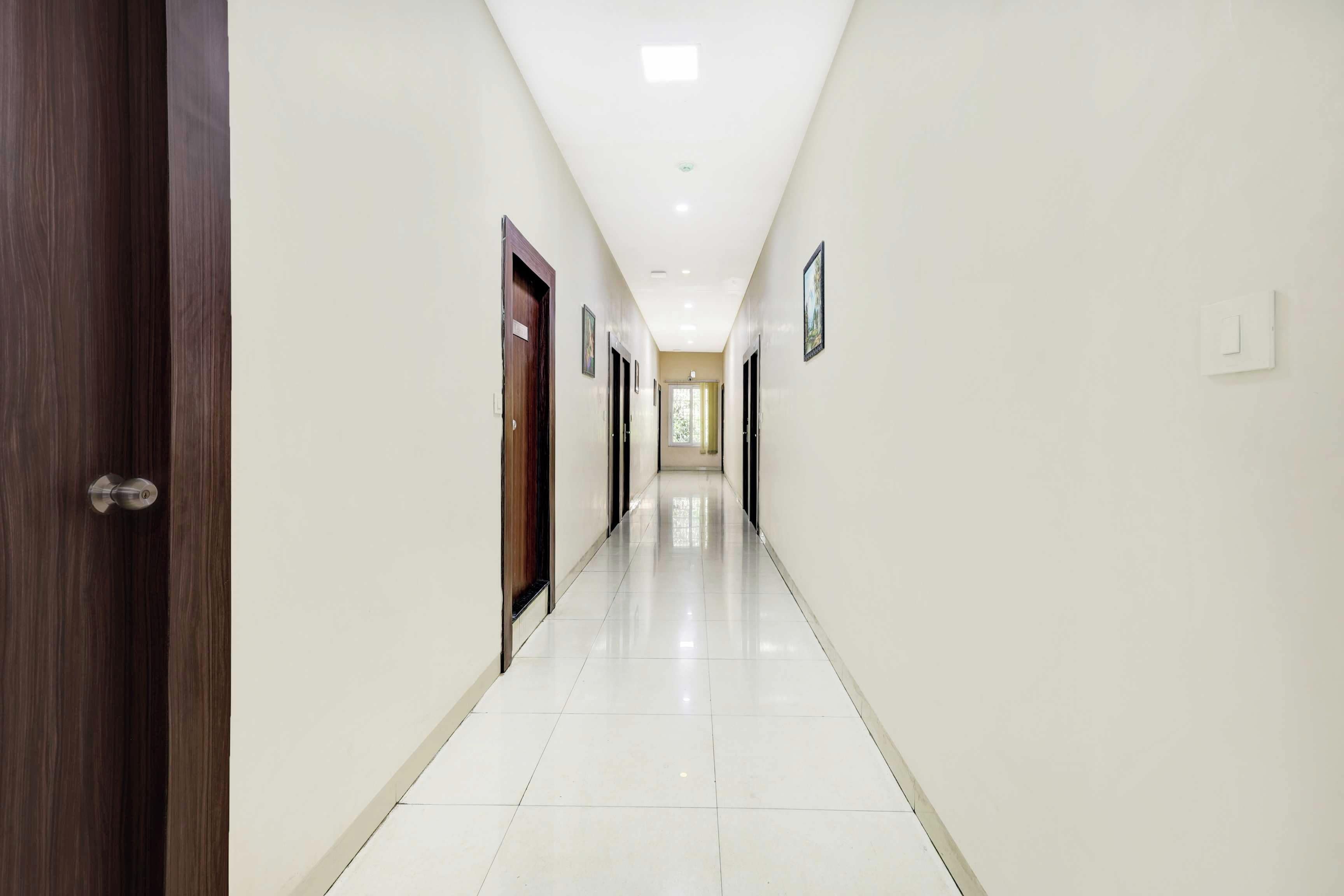A long, narrow hallway with white walls and a tiled floor, leading to a door at the end.