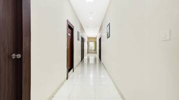 A long, narrow hallway with white walls and a tiled floor, leading to a door at the end.