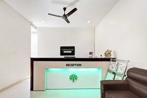 Zona de recepción con ventilador de techo, mostrador de recepción, sofá de cuero marrón y un reloj en la pared.