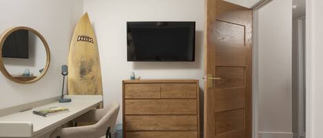 Ein Schlafzimmer mit einem Holzkasten, einem Schreibtisch mit Stuhl, einem Surfbrett, einem Fernseher und einer Tür.