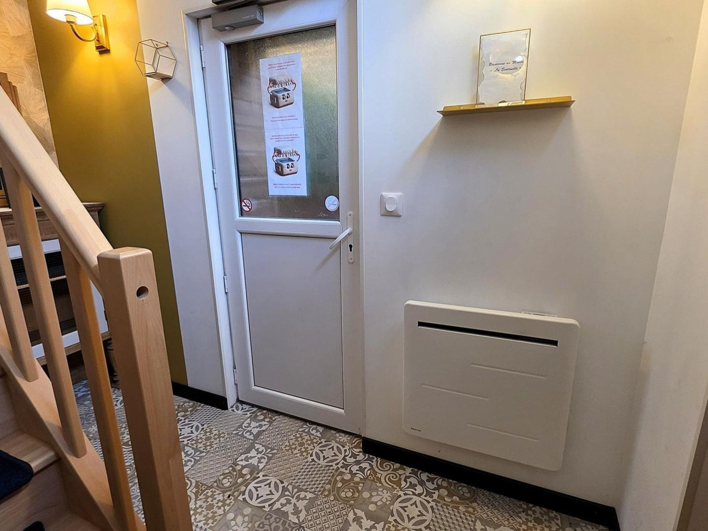 A hallway with a white door, a wall-mounted light fixture, a thermostat, and a patterned floor.