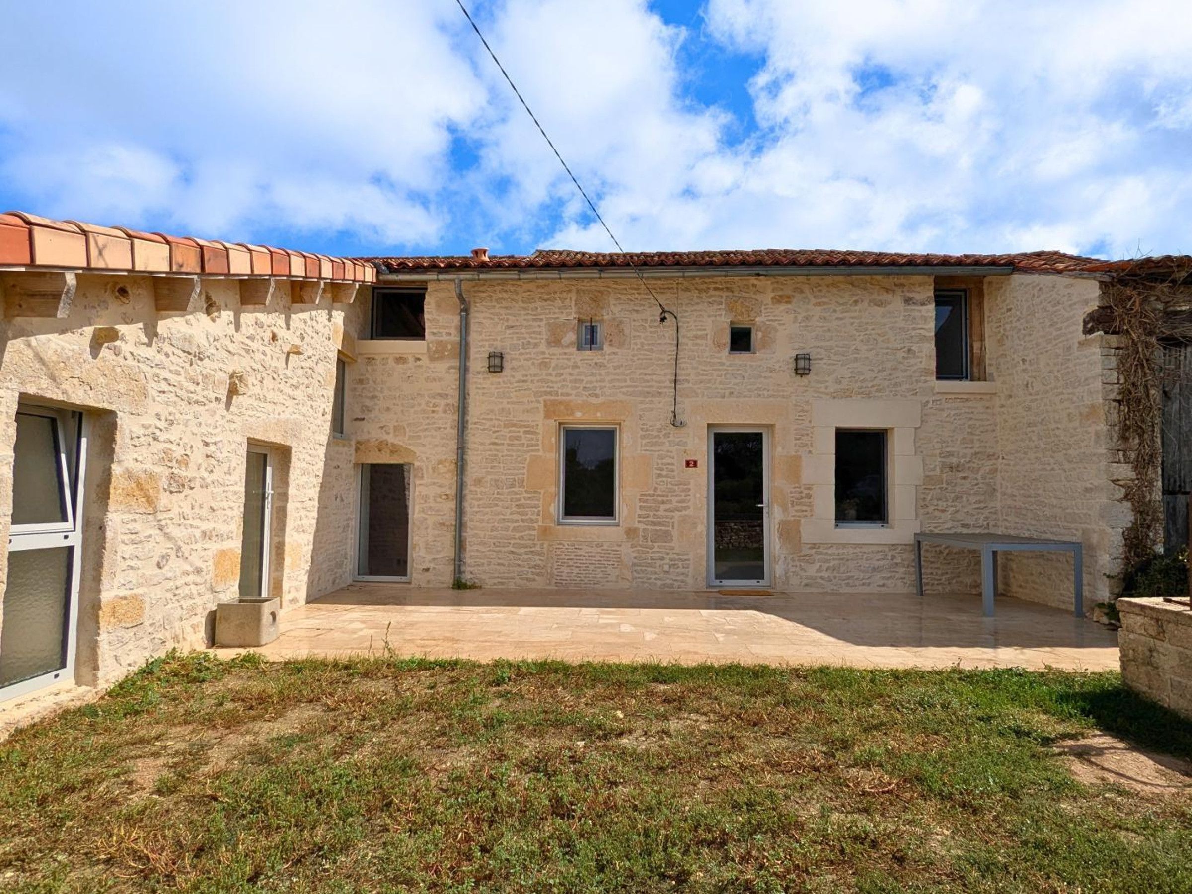 A stone building with a tiled roof, multiple windows, and a paved courtyard.