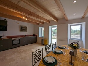 A modern kitchen with built-in appliances, a dining area with a table set for four, and large windows providing natural light. - Welcoming house, pets OK - 8 guests (Nanteuil-en-Vallée)