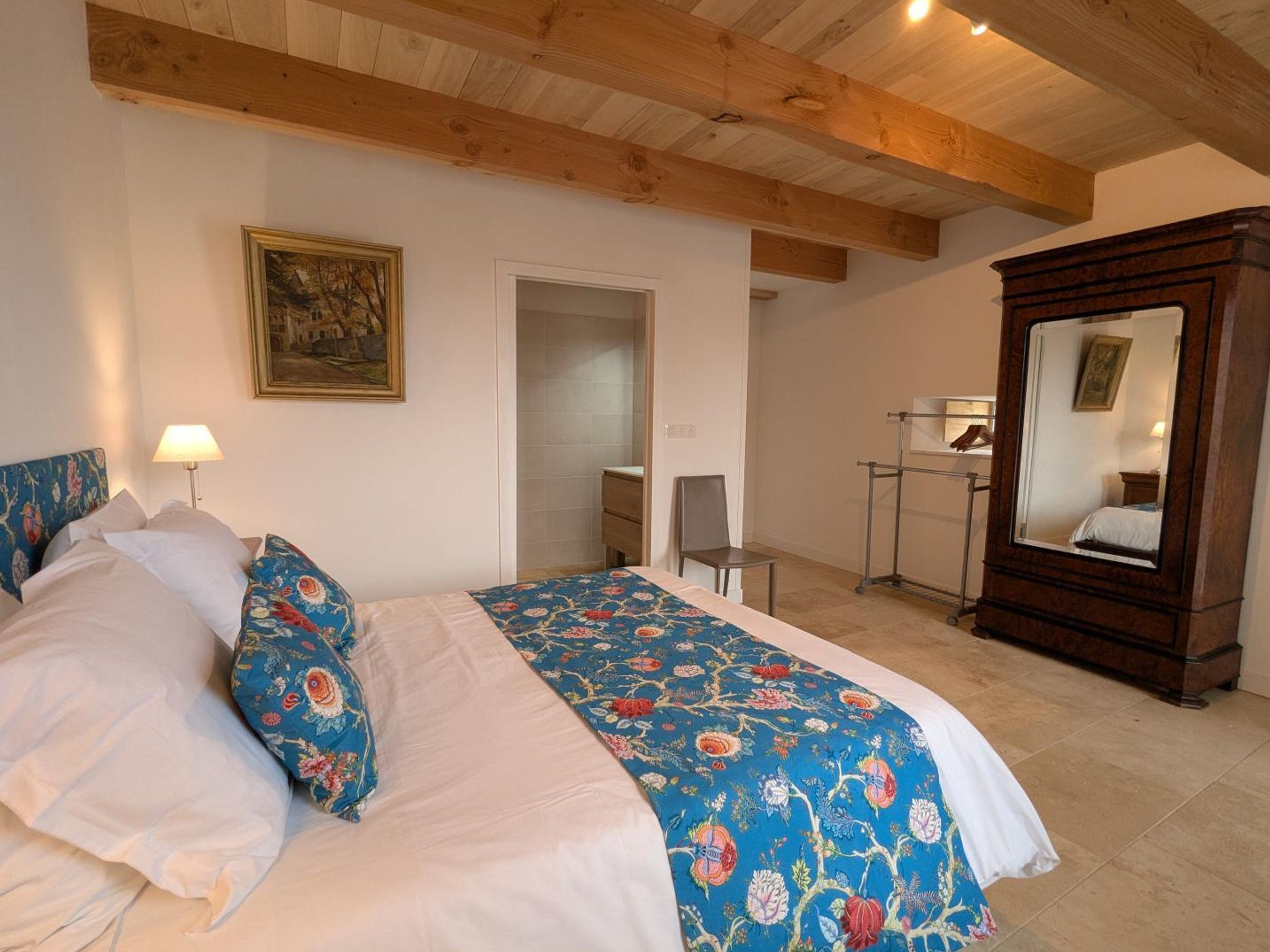 Ein Schlafzimmer mit einem Bett, einer Kommode, einem Spiegel und einer Tür zu einem weiteren Raum.