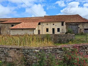 A stone building with a tiled roof, a stone wall in the foreground, and a field of tall grass. - Welcoming house, pets OK - 8 guests (Nanteuil-en-Vallée)
