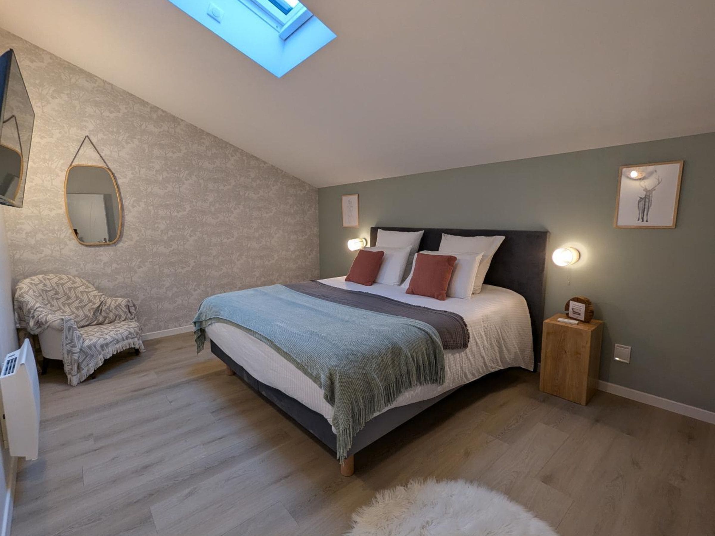 A bedroom with a bed, a chair, a mirror, and a small wooden nightstand.