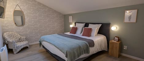 A bedroom with a bed, a chair, a mirror, and a small wooden nightstand.