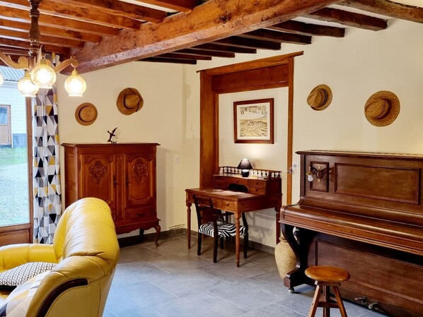 A room with a wooden ceiling, a piano, a desk with a lamp, a chair, and a cabinet. - Spacious house, preserved nature - Total serenity (CASSEL)