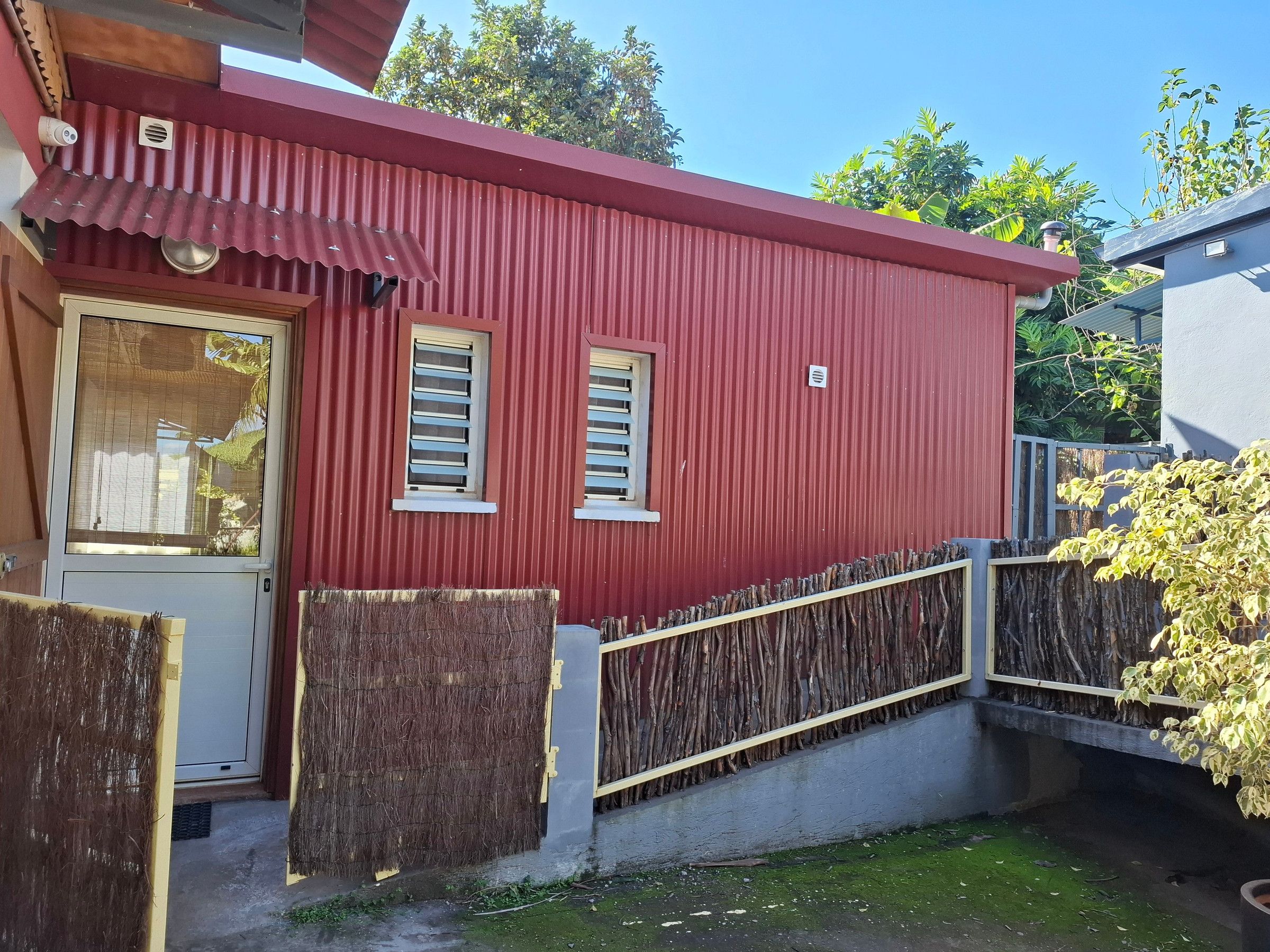 A red building with a metal roof, a door, and two windows with shutters.