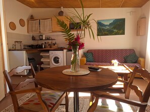 A cozy living area with a round wooden table, chairs, a sofa, a washing machine, and a painting on the wall. - Studio with stunning view - 2 guests (Saint-Joseph)