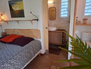 Ein Schlafzimmer mit einem Holz-Kopfteil, einem Bett mit gemusterten Betttextilien, einer Nachttischlampe, einem Wandbild und einer kleinen Holzkabine.