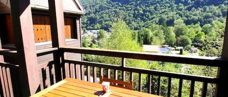 Eine Holzterrasse mit Tisch und Stühlen, mit Blick auf ein bewaldetes Tal und Berge.