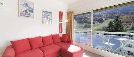 A modern living room with a red sofa, a small table with magazines, and a large window offering a view of a mountainous landscape.