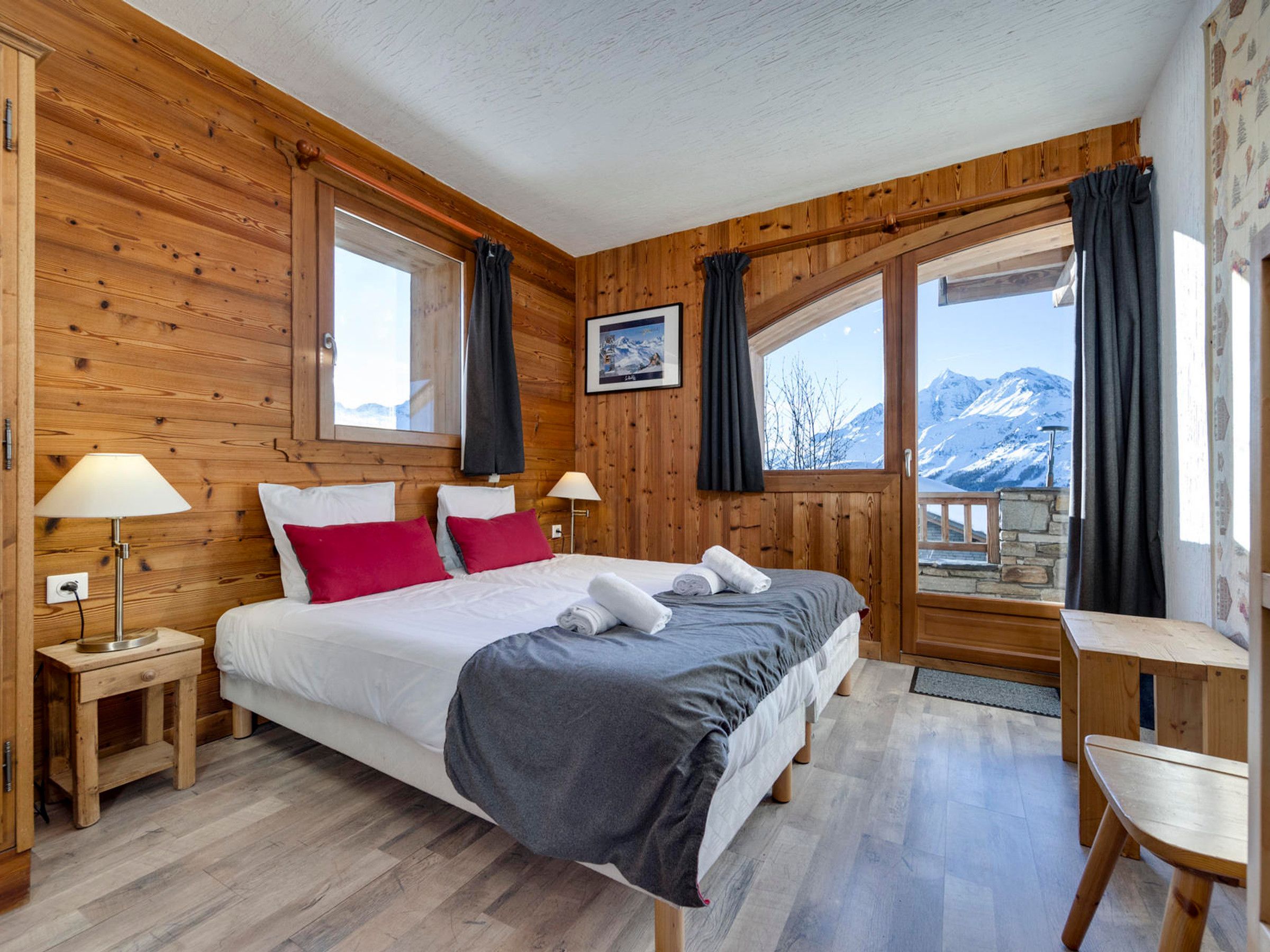 Een slaapkamer met houten lambrisering, een bed, twee nachtkastjes, een bureau en uitzicht op bergen.