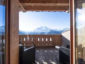 Eine Holzterrasse mit Korbstühlen, Blick auf schneebedeckte Berge und einem Hollergazier mit Baumdekorationen.