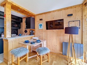 A compact wooden room with a kitchen area, a dining table with blue tableware, and a floor lamp. - Cozy ski-in/ski-out apartment, south-facing balcony (Les Menuires)