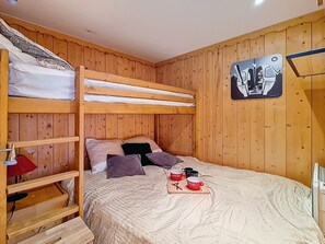 A bunk bed room with a wooden headboard, a small table with cups, and a wall-mounted artwork. - Cozy ski-in/ski-out apartment, south-facing balcony (Les Menuires)