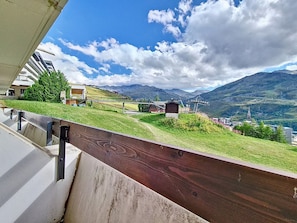 A balcony with a view of a mountainous landscape, a ski lift, and a small building. - Cozy ski-in/ski-out apartment, south-facing balcony (Les Menuires)