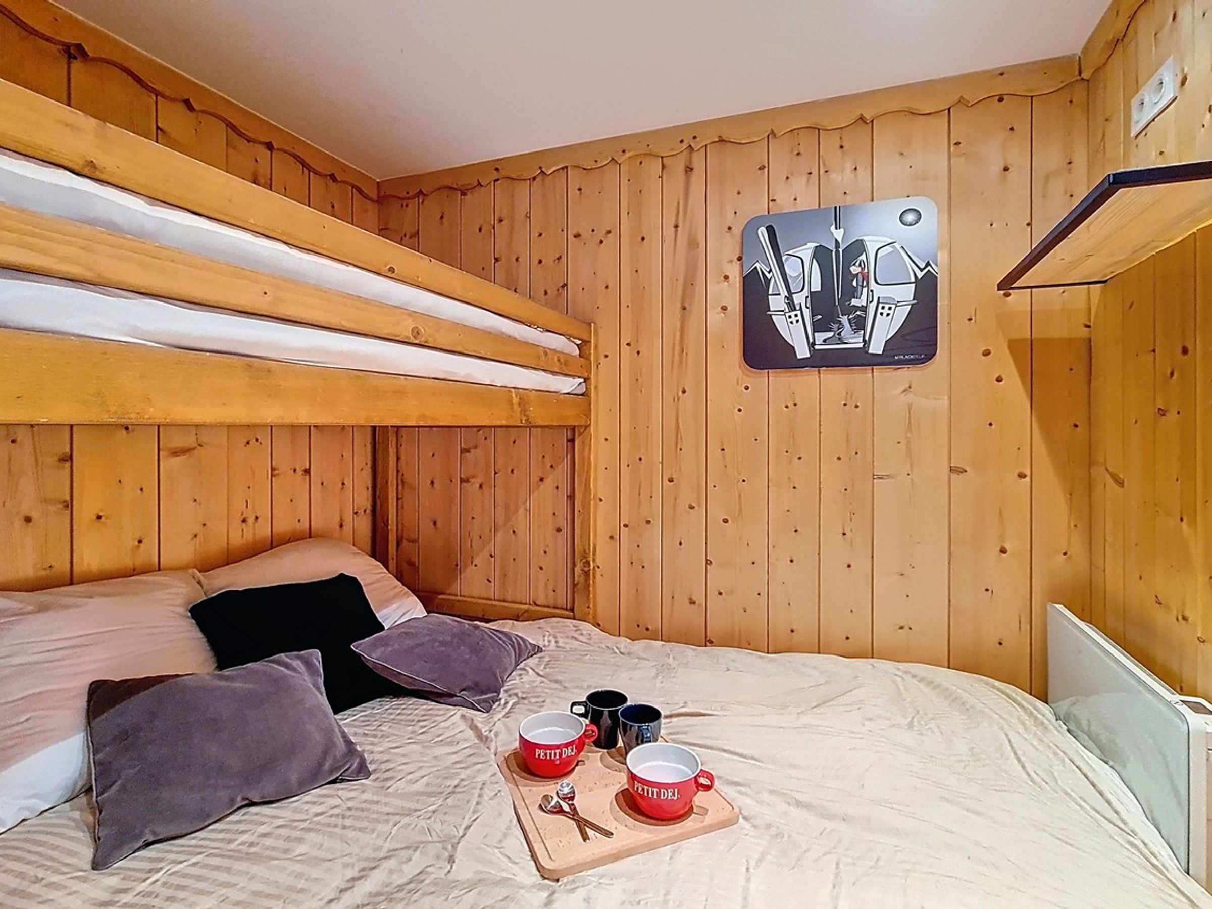 Een slaapkamer met stapelbed, houten wanden, een bed met kussens en een kunstwerk aan de muur.