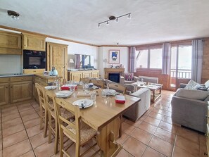 A spacious dining area with wooden furniture, a fireplace, and a large window providing natural light. - Spacious 75m² Apartment, Ski-in/Ski-out, Southwest Balcony (Les Menuires)
