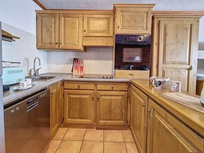 A kitchen with wooden cabinets, a built-in oven, and a dishwasher. - Spacious 75m² Apartment, Ski-in/Ski-out, Southwest Balcony (Les Menuires)