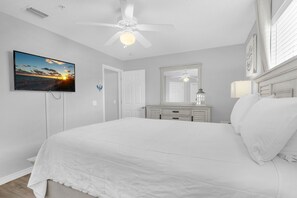 Ein Schlafzimmer mit einem Bett, einem Deckenventilator, einem Fernseher, einem Schminktisch und einem Spiegel.