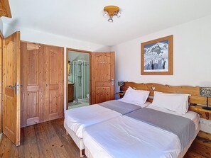A room with two beds, wooden doors, a shower, and a framed picture on the wall. - Spacious apartment with pool access and terrace, ski-in/ski-out (Les Menuires)