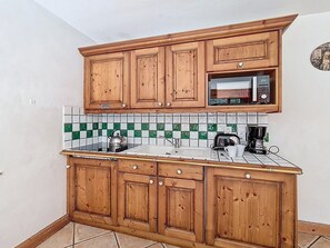 Una cocina con armarios de madera, microondas, hervidor de agua y cafetera.
