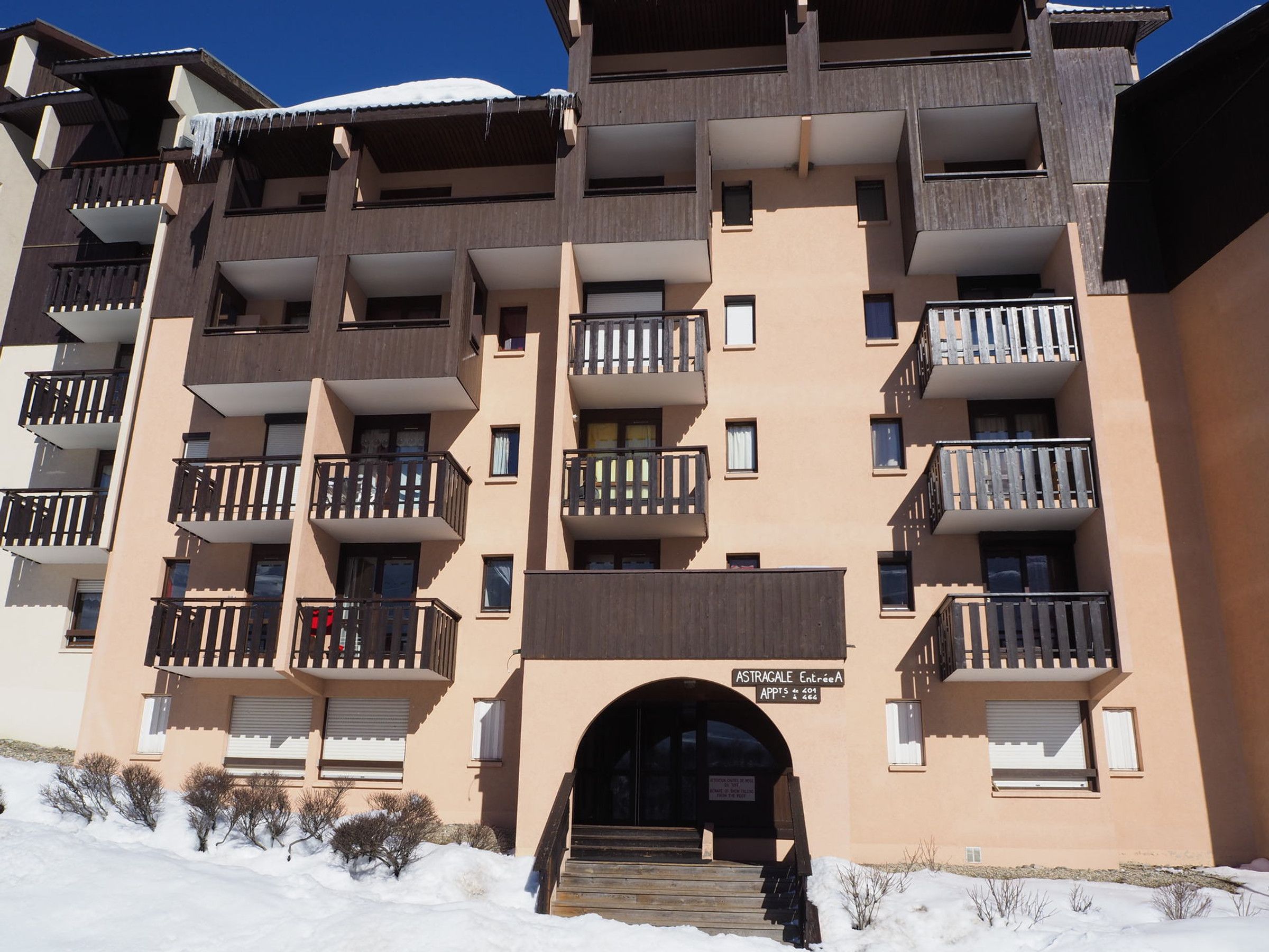 Um hotel de vários andares com varandas, uma entrada com degraus e uma placa indicando "ASTRAGALE Entrée".