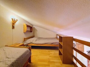 Eine kleine, einförmige Unterkunft mit Schlafboden, geneigter Decke, einer an der Wand befestigten Ablage und einem schlichten Boden.