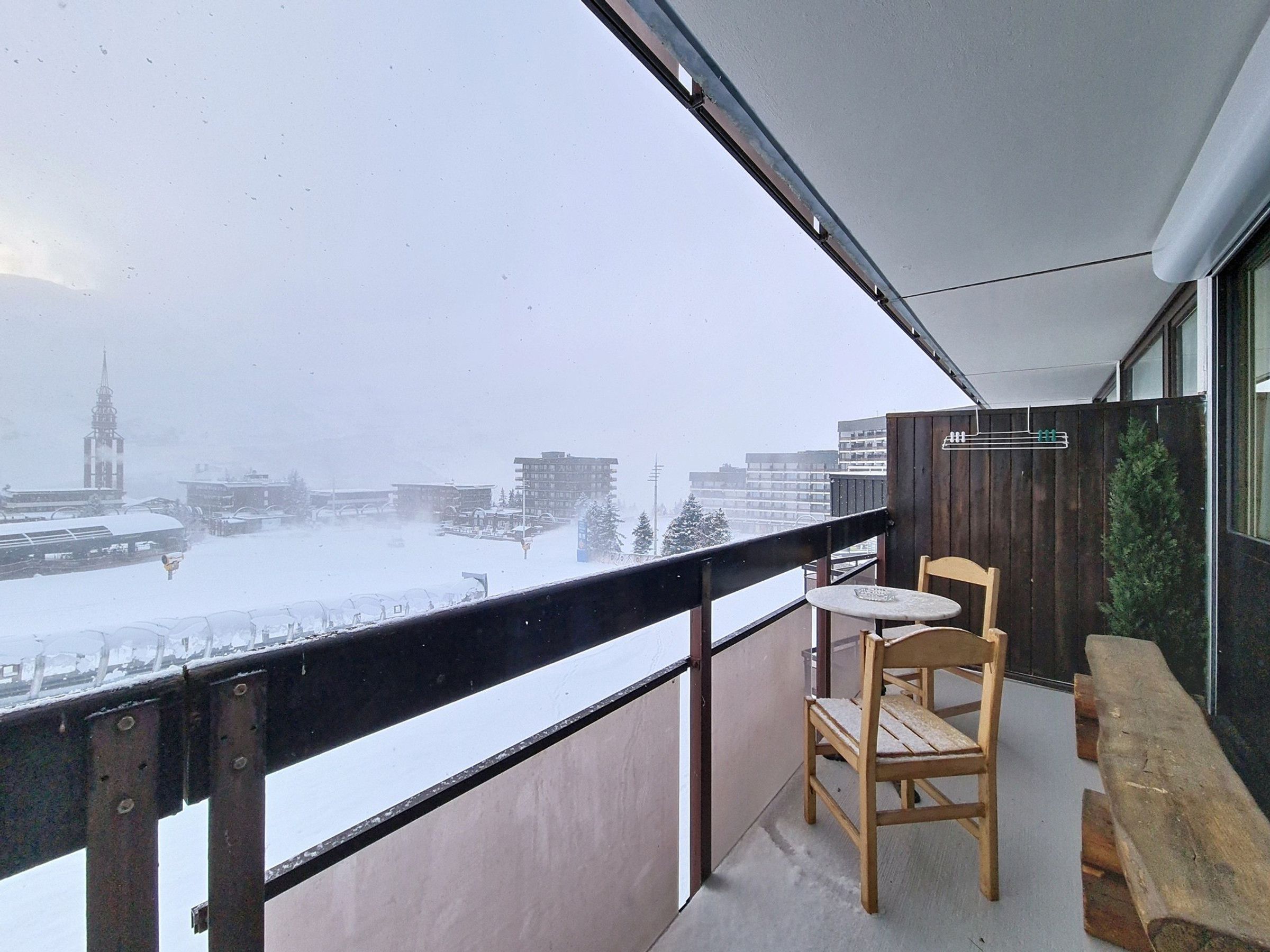 Een balkon met een houten bankje en tafel, met uitzicht op een besneeuwd stadsbeeld met gebouwen en een trein.
