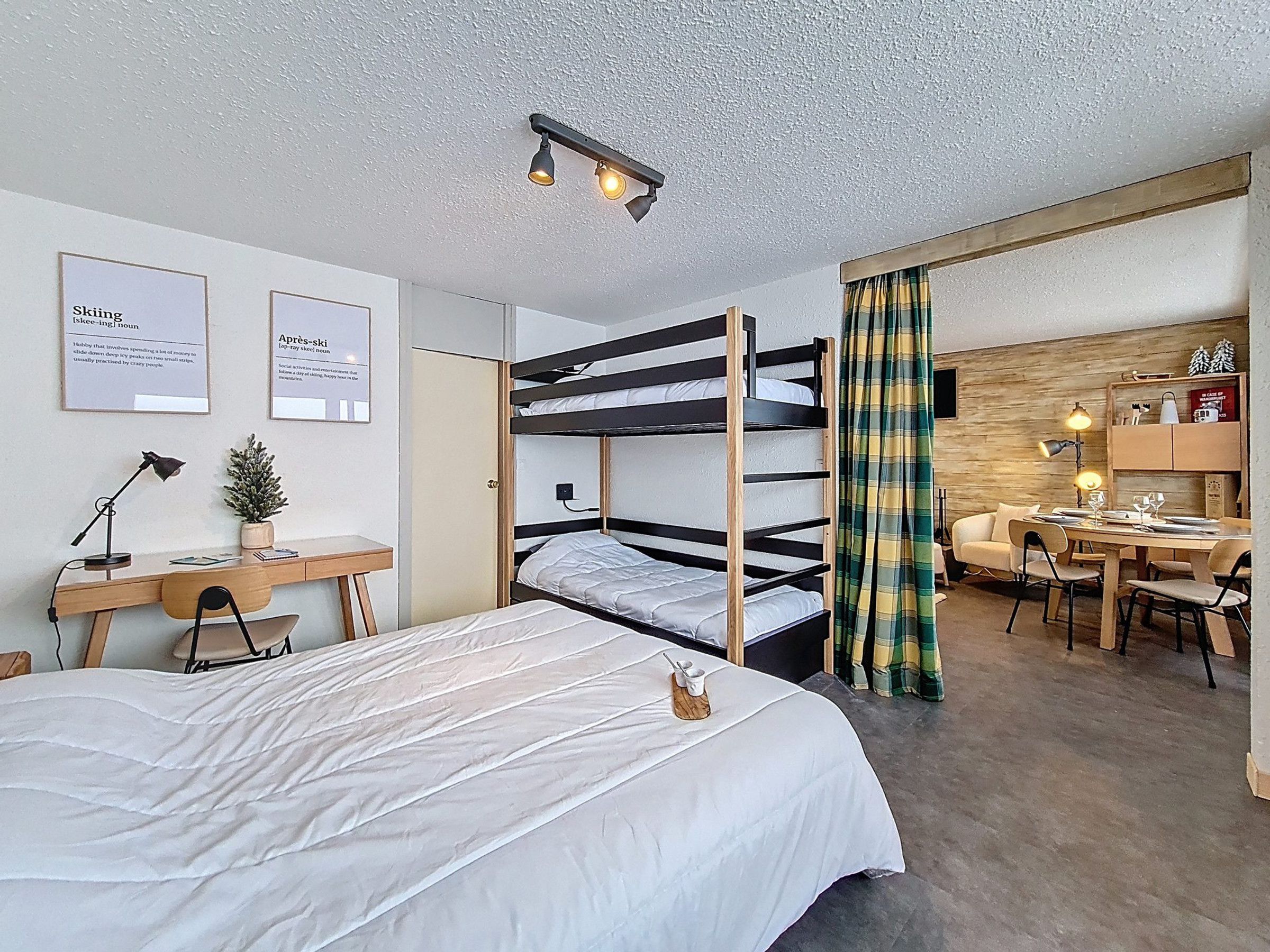 A hotel room with bunk beds, a desk, a chair, a lamp, and a small plant.