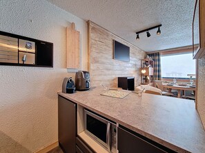 A compact kitchen with a microwave, coffee maker, and a small dining table with chairs. - Bright apartment at the foot of the slopes - 4 guests (Les Menuires)
