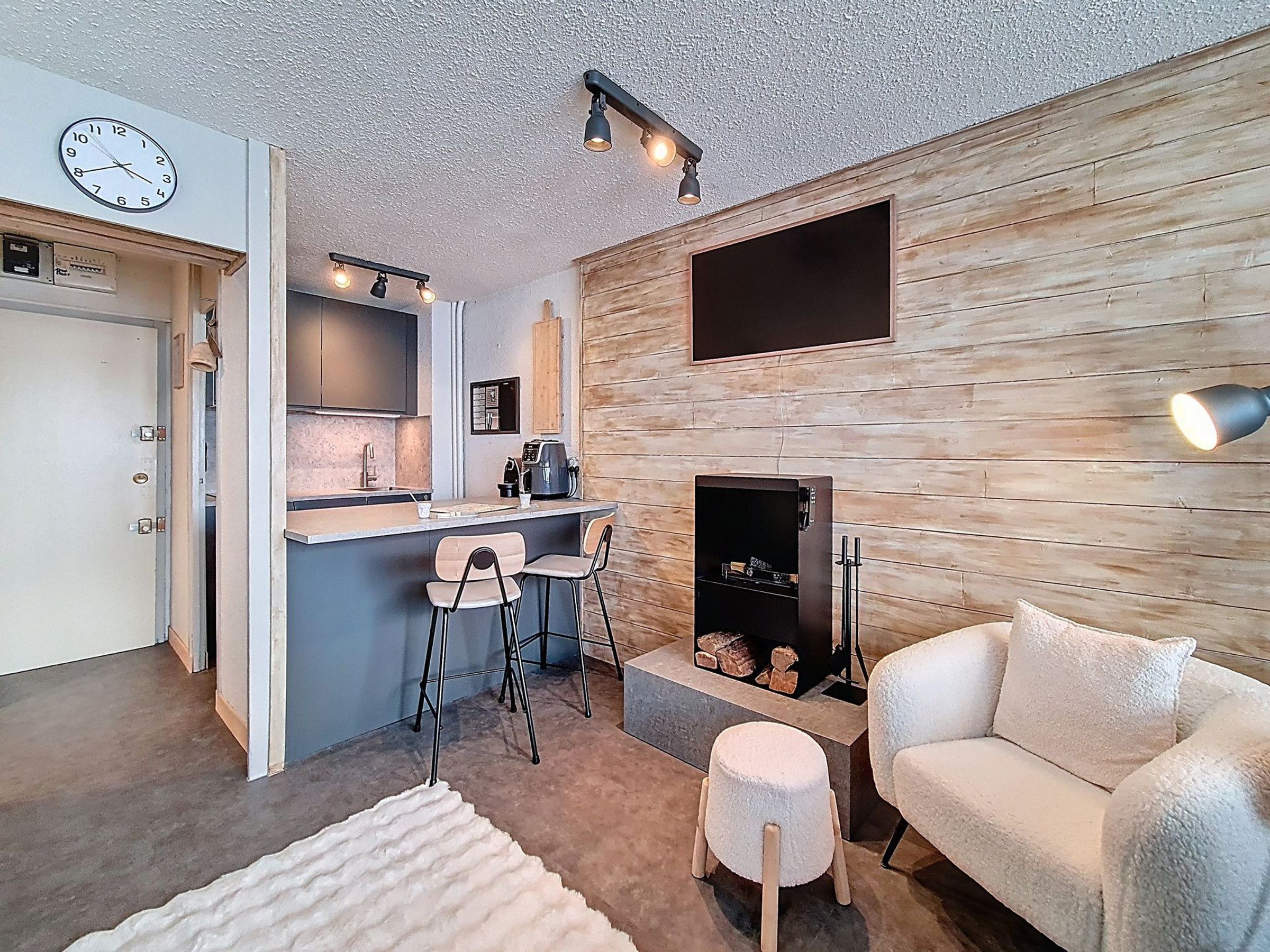 A modern living room with a fireplace, a kitchen with a bar area, and a clock on the wall.