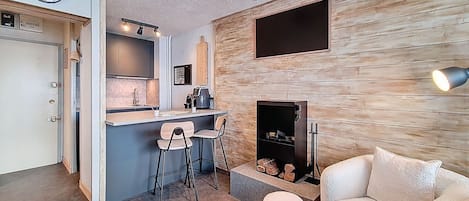 A modern living room with a fireplace, a kitchen with a bar area, and a clock on the wall.