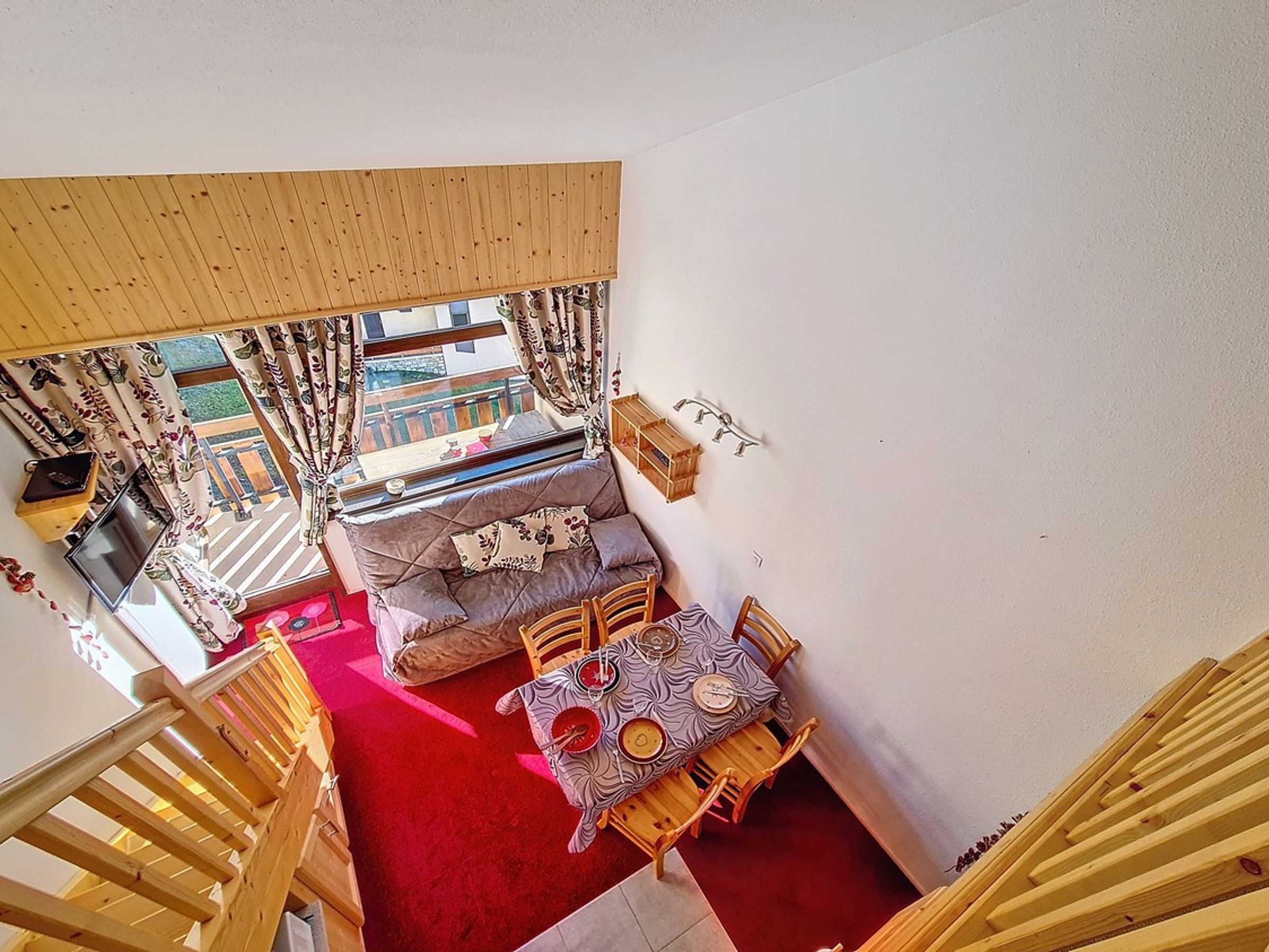 A room with a red carpet, a sofa, a table with chairs, and a wooden staircase.
