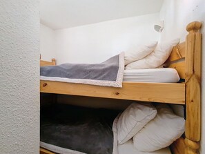 A bunk bed with a grey blanket and white pillows, wooden headboard, and a white wall. - Two-room apartment, mountain view - 4 guests (Les Menuires)